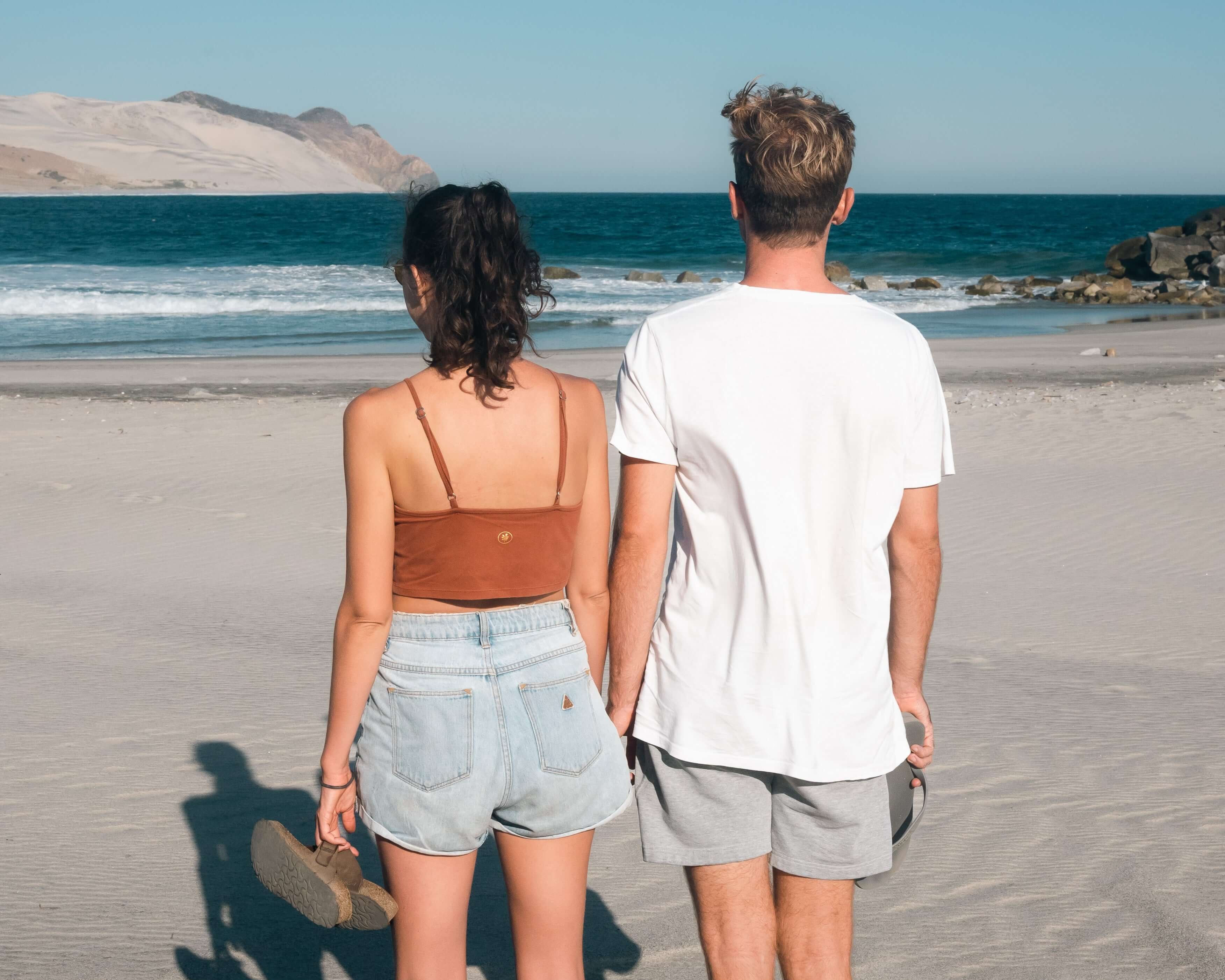 Couple enjoying a sunny day on the beach, looking out at the ocean waves.