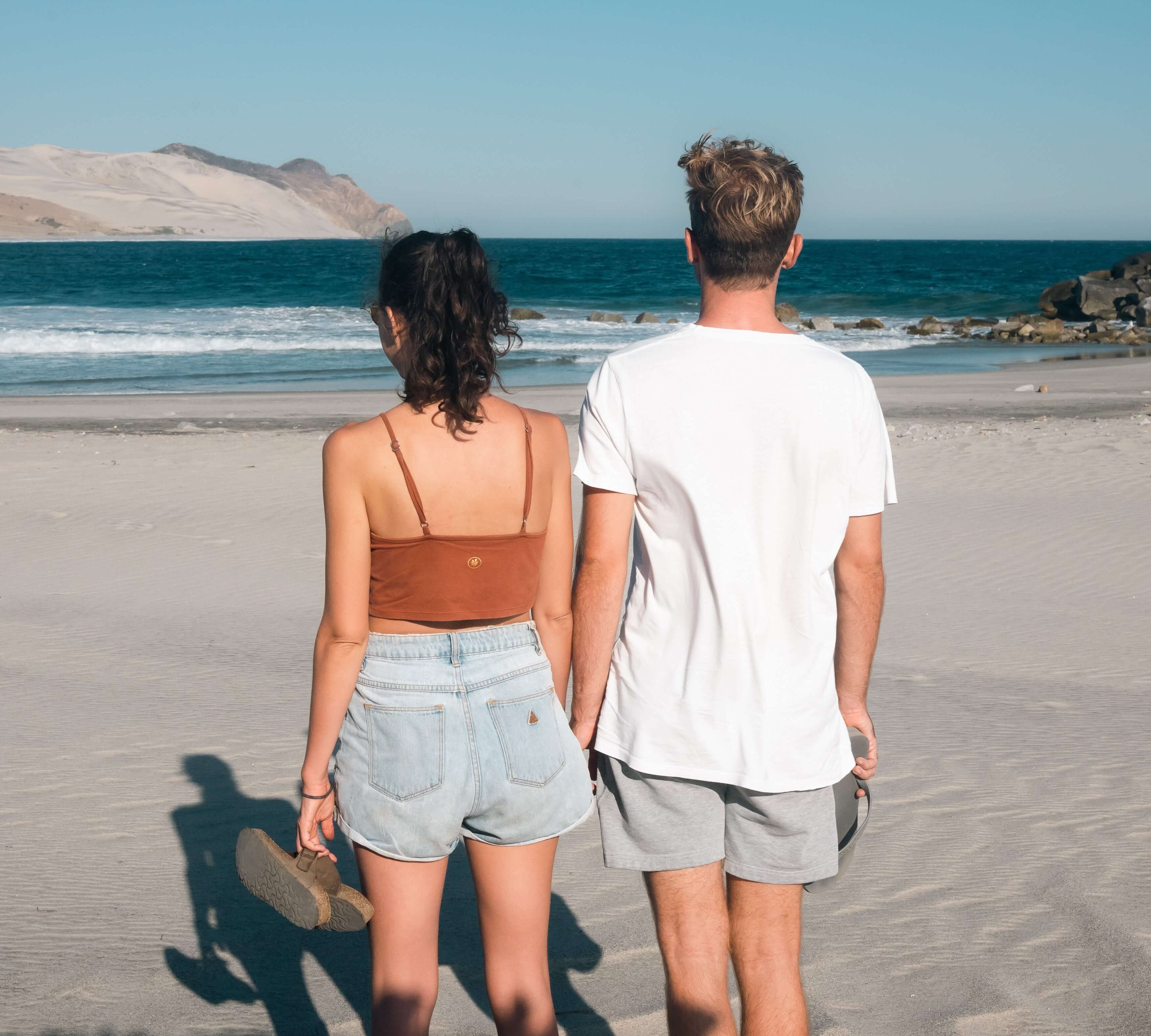 Couple enjoying a sunny day on the beach, looking out at the ocean waves.