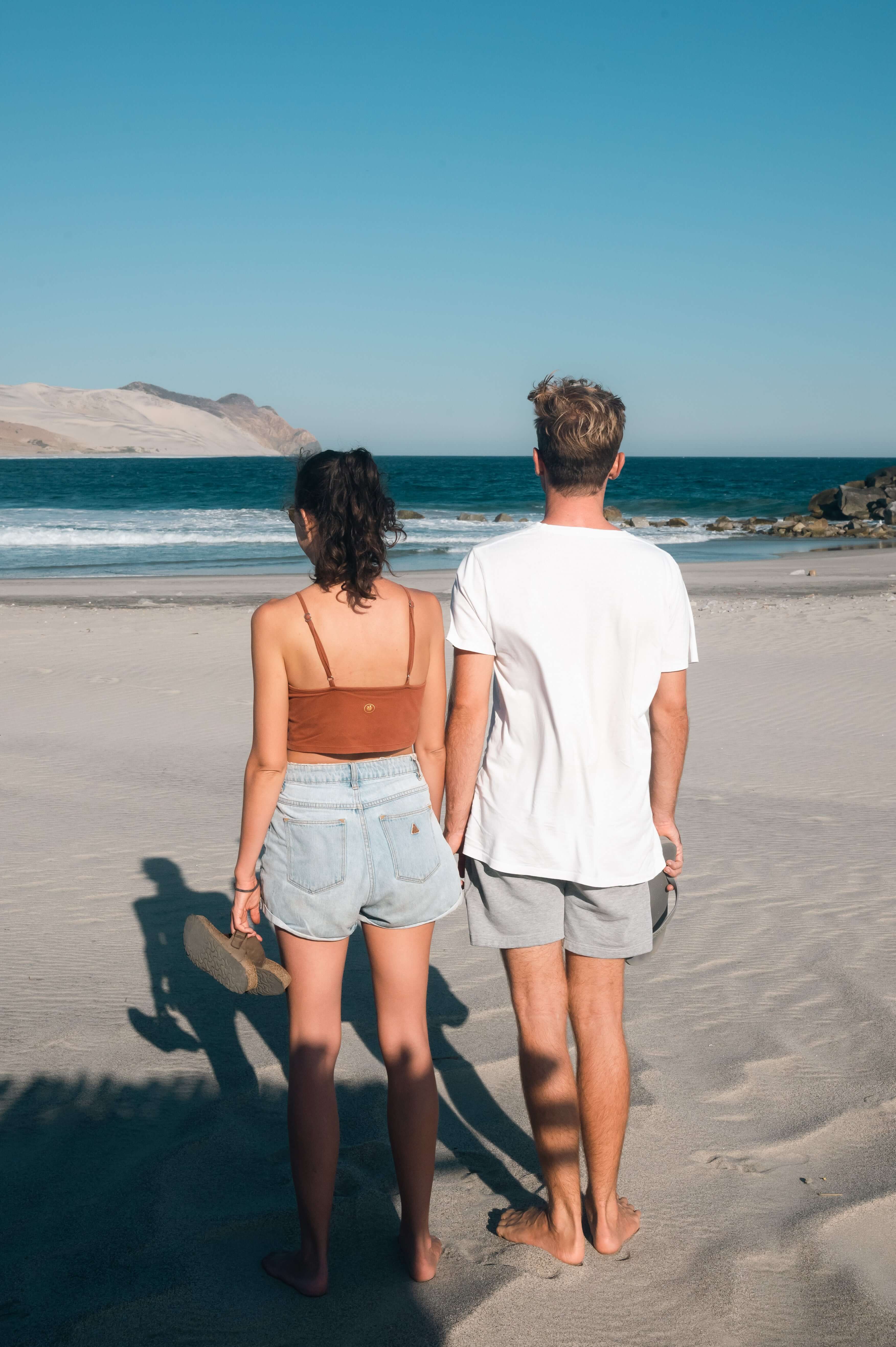 Couple enjoying a sunny day on the beach, looking out at the ocean waves.