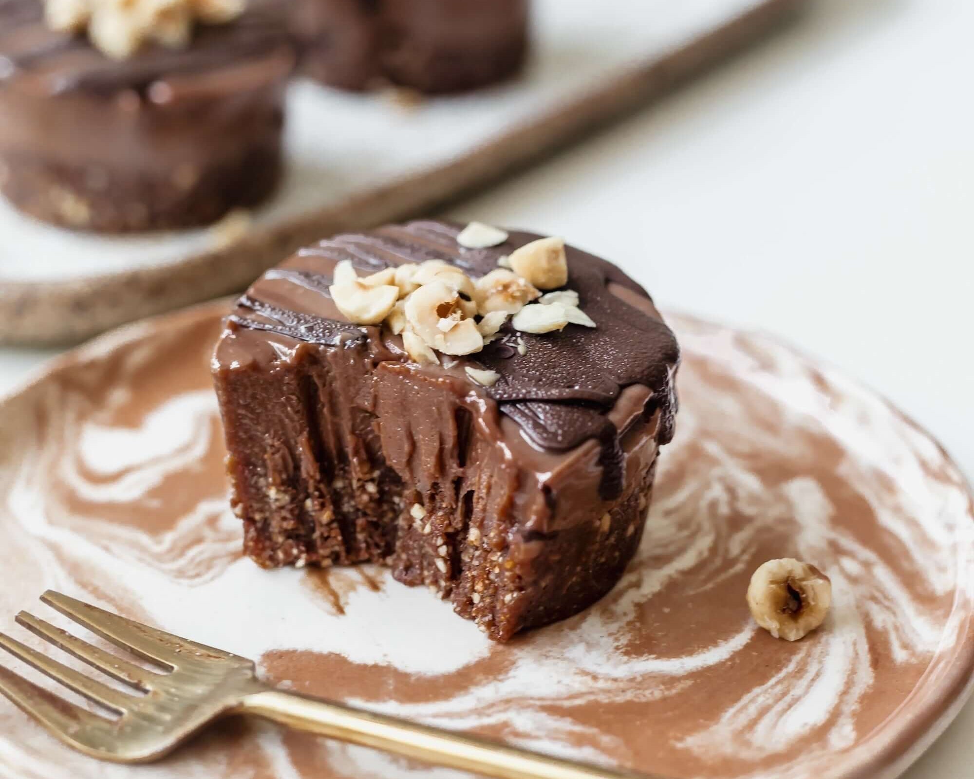 Vegan mini chocolate hazelnut cheesecake on a plate, topped with crushed hazelnuts and chocolate glaze.