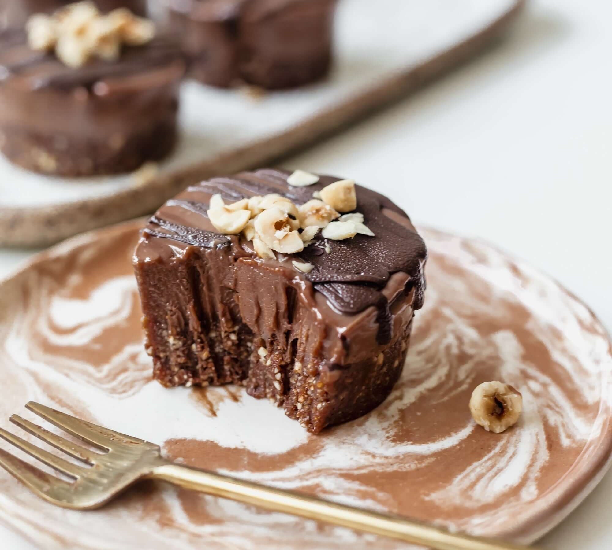 Vegan mini chocolate hazelnut cheesecake on a plate, topped with crushed hazelnuts and chocolate glaze.