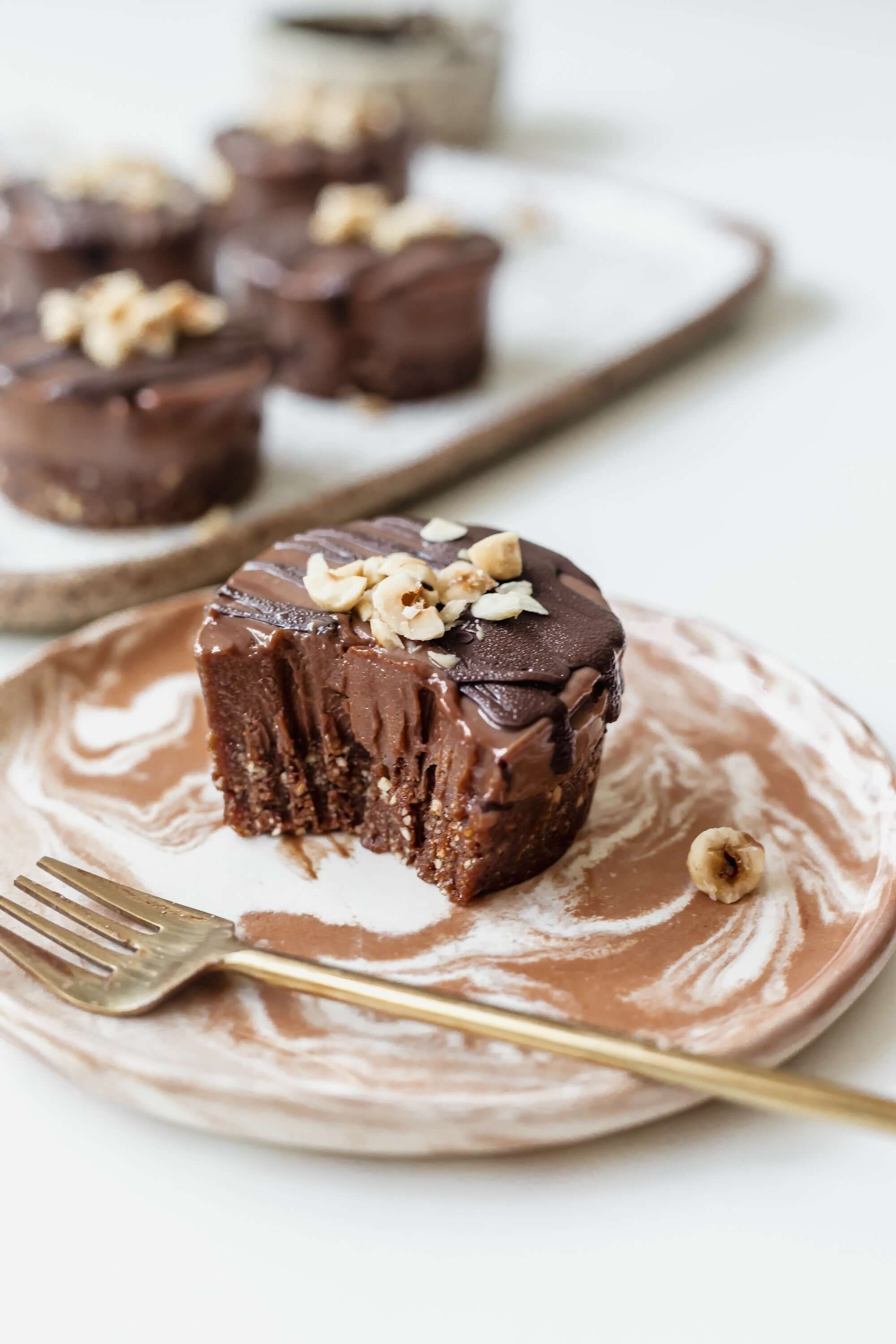 Vegan mini chocolate hazelnut cheesecake on a plate, topped with crushed hazelnuts and chocolate glaze.