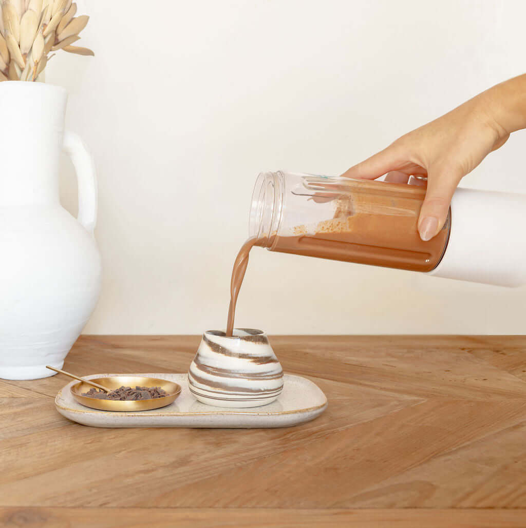 Hand pouring ceremonial cacao drink into a stylish cup on a wooden table, highlighting cacao vs coffee and health benefits.