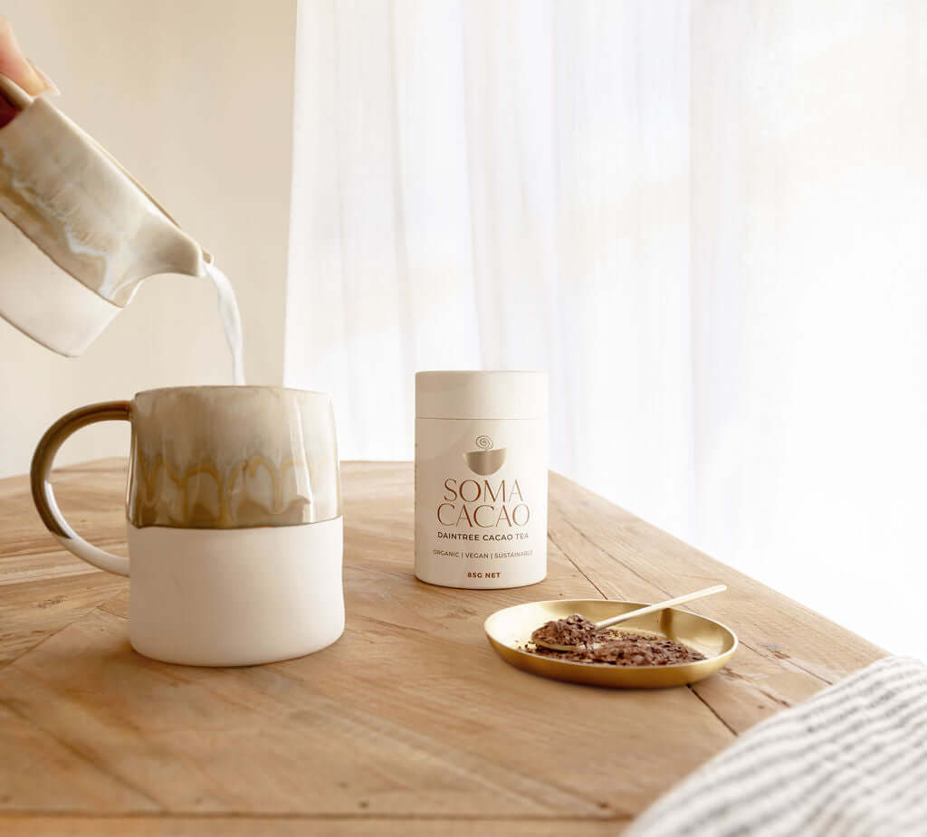 Daintree Cacao Tea and Brass Scoop next to a steaming mug for a ceremonial cacao experience.