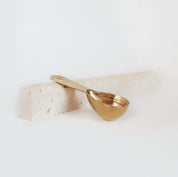 Gold measuring scoop on a natural stone block, perfect for ceremonial cacao rituals. Premium quality accessory.