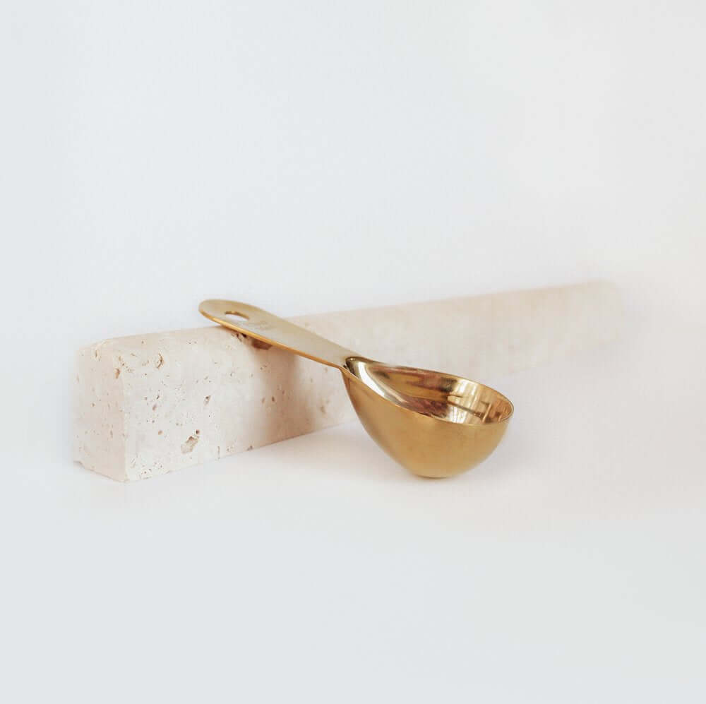 Gold measuring scoop on a natural stone block, perfect for ceremonial cacao rituals. Premium quality accessory.